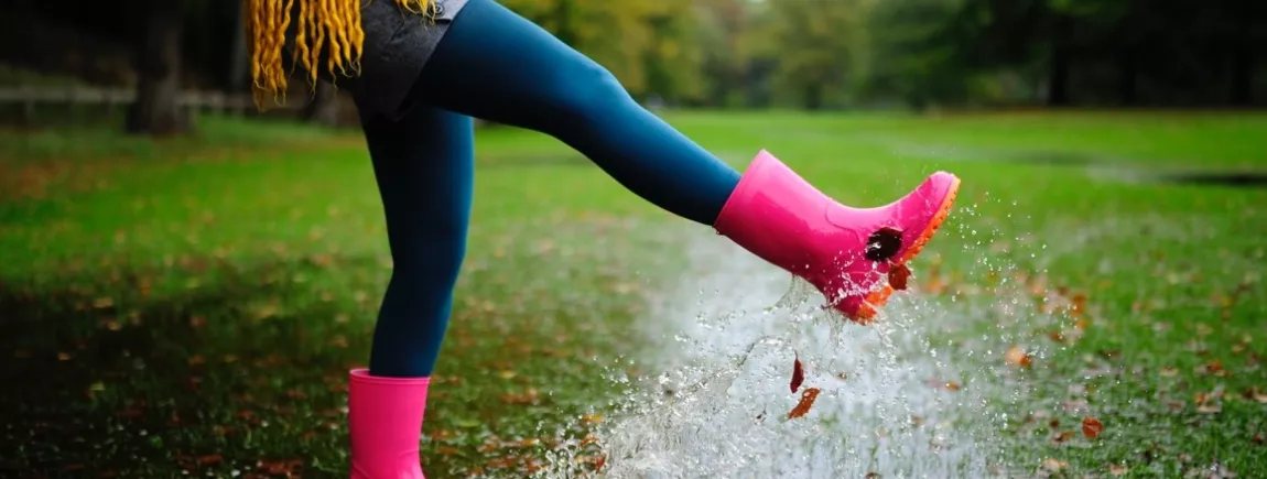 Une femme vêtue de bottes de pluie saute dans des flaques d’eau