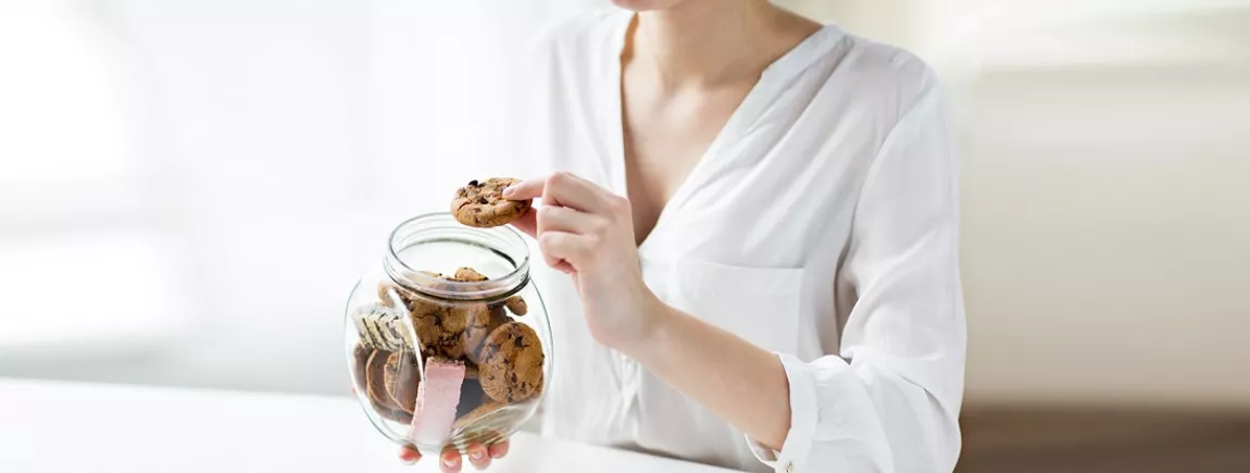 Une femme mange des cookies rangés dans un bocal