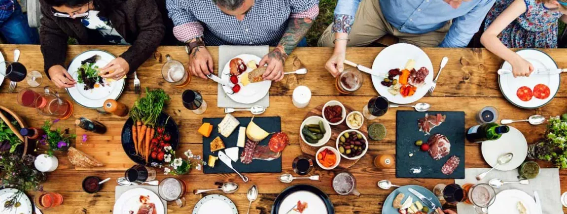 Un groupe de convives attablés autour d’une table en bois garnie de produits culinaires